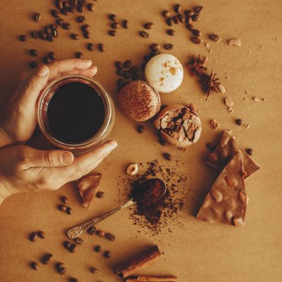 Hands holding glass cup with fresh coffee and roasted beans